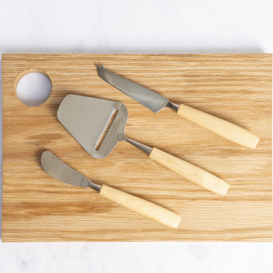 A set of 3 bjorklund cheese knives on a wooden chopping board.