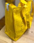 A London Cheesemongers yellow tote bag on a wooden table.