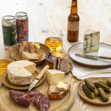 A table laid with selection plates of cheeses, pickles, charcuterie and beer.