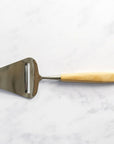 A wooden handled cheese slicer on a marble work top.