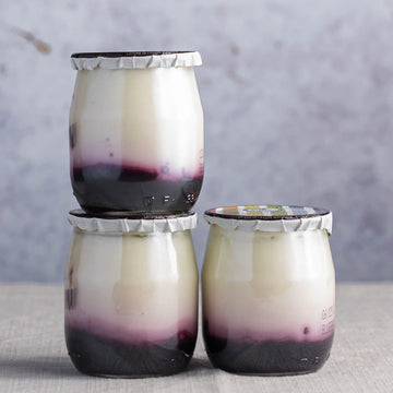 Three pots of blueberry compote yoghurt in glass jars.