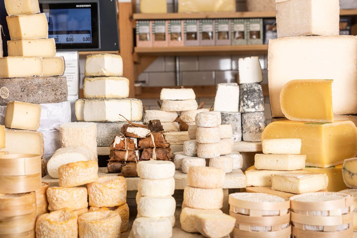 Cheeses of different shapes sizes and colours on a shop counter.