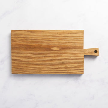 A small rectangular wooden chopping board with a small handle at one end on top of a marble worktop.