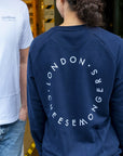 The back of a lady wearing a navy sweatshirt, with a round London Cheesemongers logo on the back, standing next to a man wearing a white t-shirt.