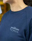 A lady wearing a navy sweatshirt, with a straight London Cheesemongers and knife logo printed on the breast.