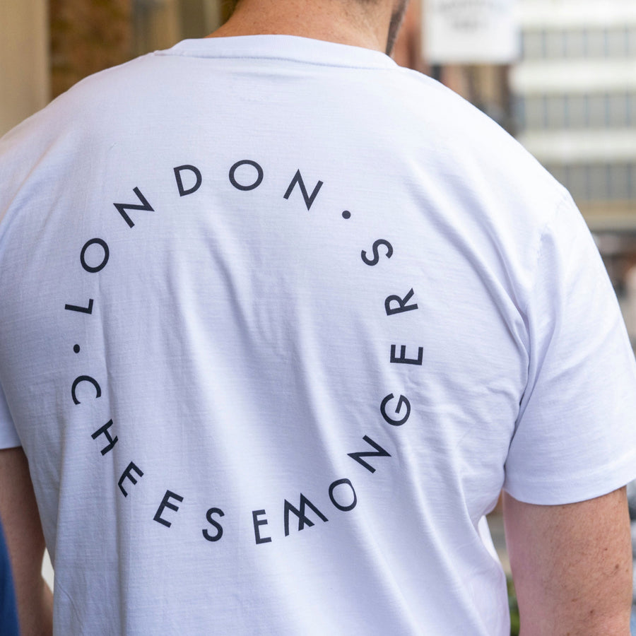 The back of a man wearing a white t-shirt with a printed round London Cheesemongers logo.