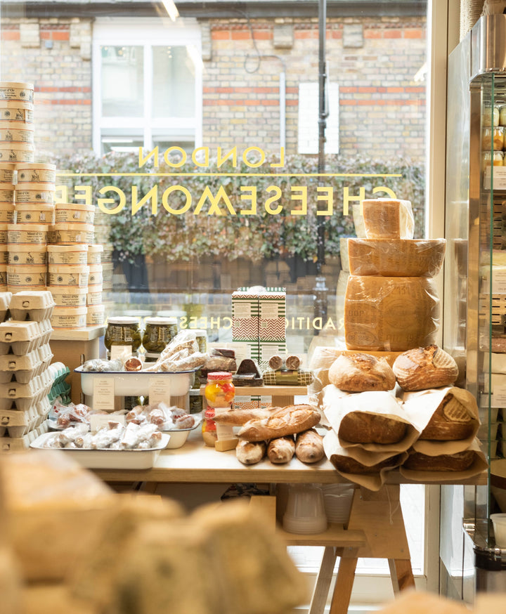 Table in the shop window of London Cheesemongers containing eggs, cheese, bread, charcuterie and other provisions.