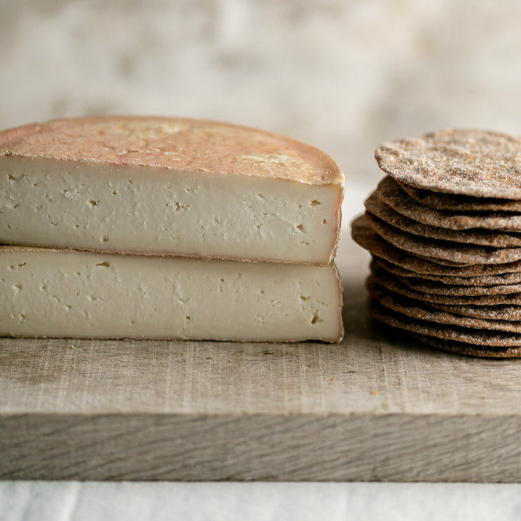 A cut Riseley ewe's milk cheese with some savoury biscuits on a wooden board.