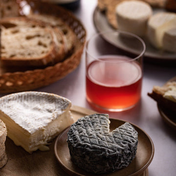 A glass of wine and a selection of cheeses on plates and a wooden board.