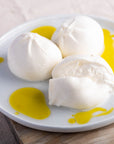 Balls of whole and cut Burrata cheese on a plate drizzled with some olive oil.