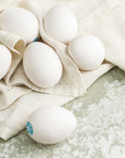 Some white Cacklebean hen's eggs on a table cloth on a worktop.