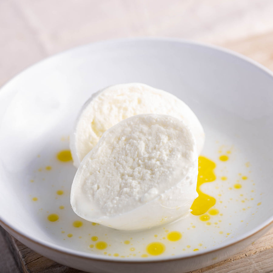 A cut Mozzarella cheese on a plate drizzled with some olive oil.