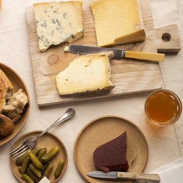 A selection of cheese, accompaniments and wine on plates and a wooden board.