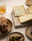 A selection of bread, cheese and cornichons on plates and a wooden board.