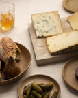 A selection of bread, cheese and cornichons on plates and a wooden board.