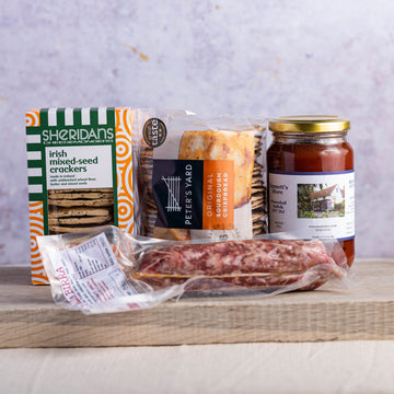 A selection of biscuits for cheese, a salami and a jar of chutney on a wooden board.