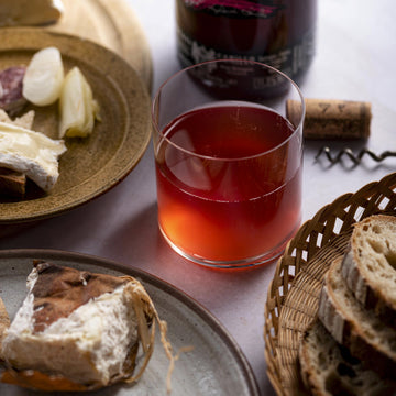 A glass of rosé wine with cheese, bread and accompaniments on plates in baskets.