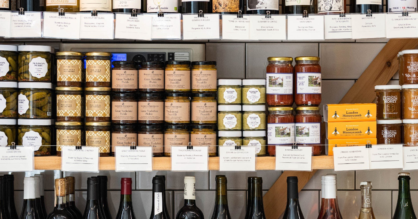 A wooden shelf containing various sized jars of chutneys, pickles and honey