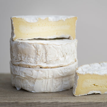 Stack of cheese wheels with one wheel cut open on a wooden surface