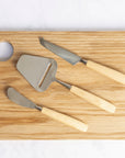 A set of 3 bjorklund cheese knives on a wooden chopping board.