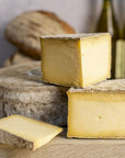 Whole and large cuts of Caerphilly cheese on a wooden chopping board.