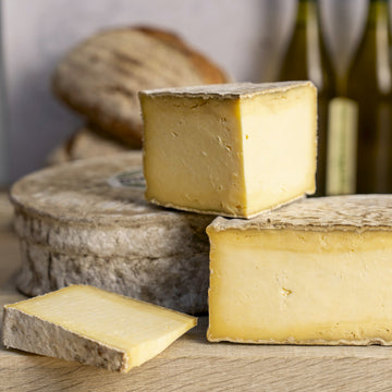 Whole and large cuts of Caerphilly cheese on a wooden chopping board.