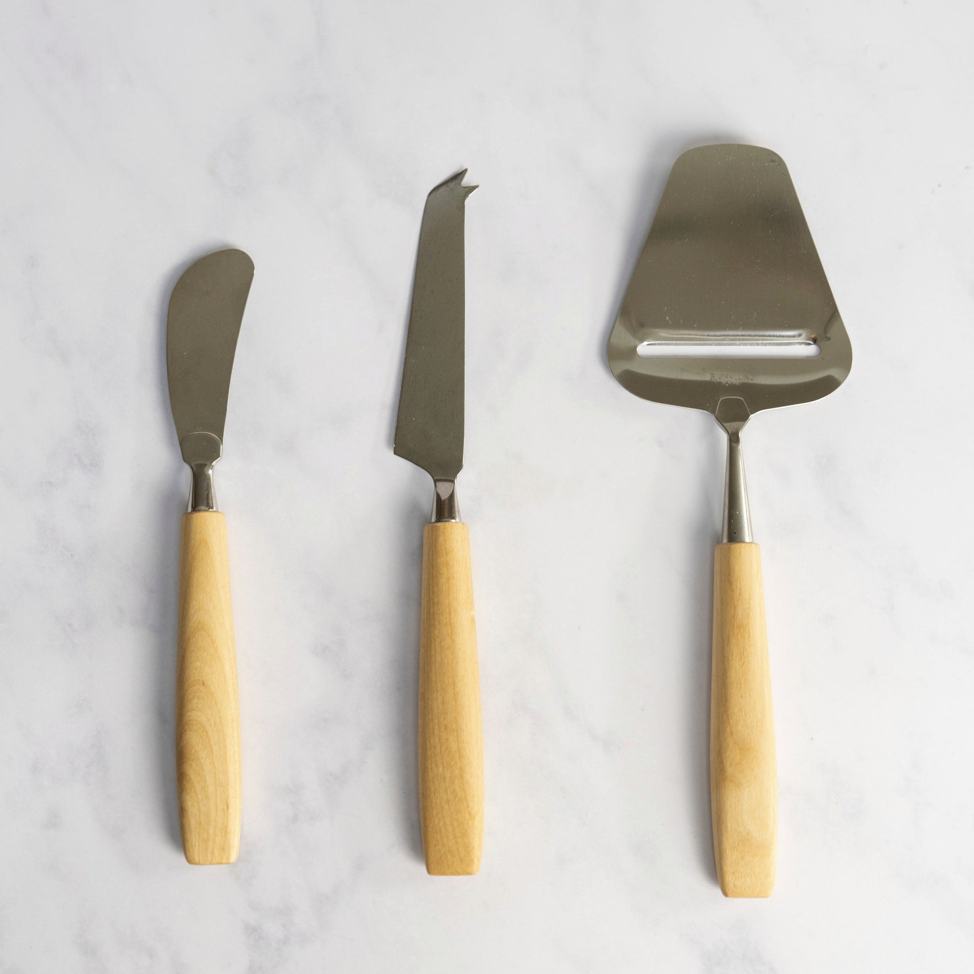 A set of three Bjorklund knives for cheese arranged vertically on a marble work top.