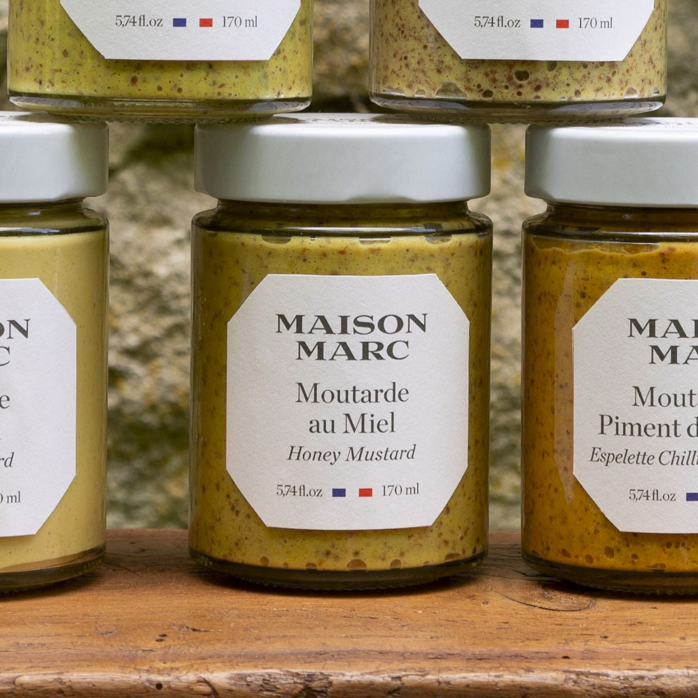 Jars of Maison Marc honey mustard on a wooden surface with a blurred natural background