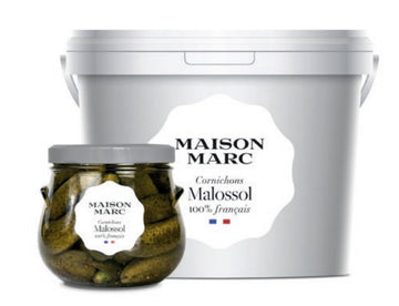 A large white bucket and glass jar of Maison March cornichons.