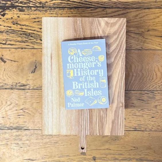 A paperback copy of Ned Palmer's 'A cheesemonger's history of the British Isles' book, on a wooden chopping board.