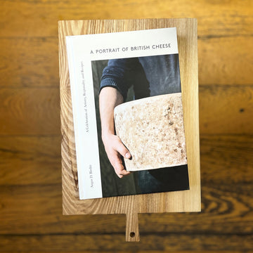 A hardback copy of 'a portrait of british cheese' on a wooden board.