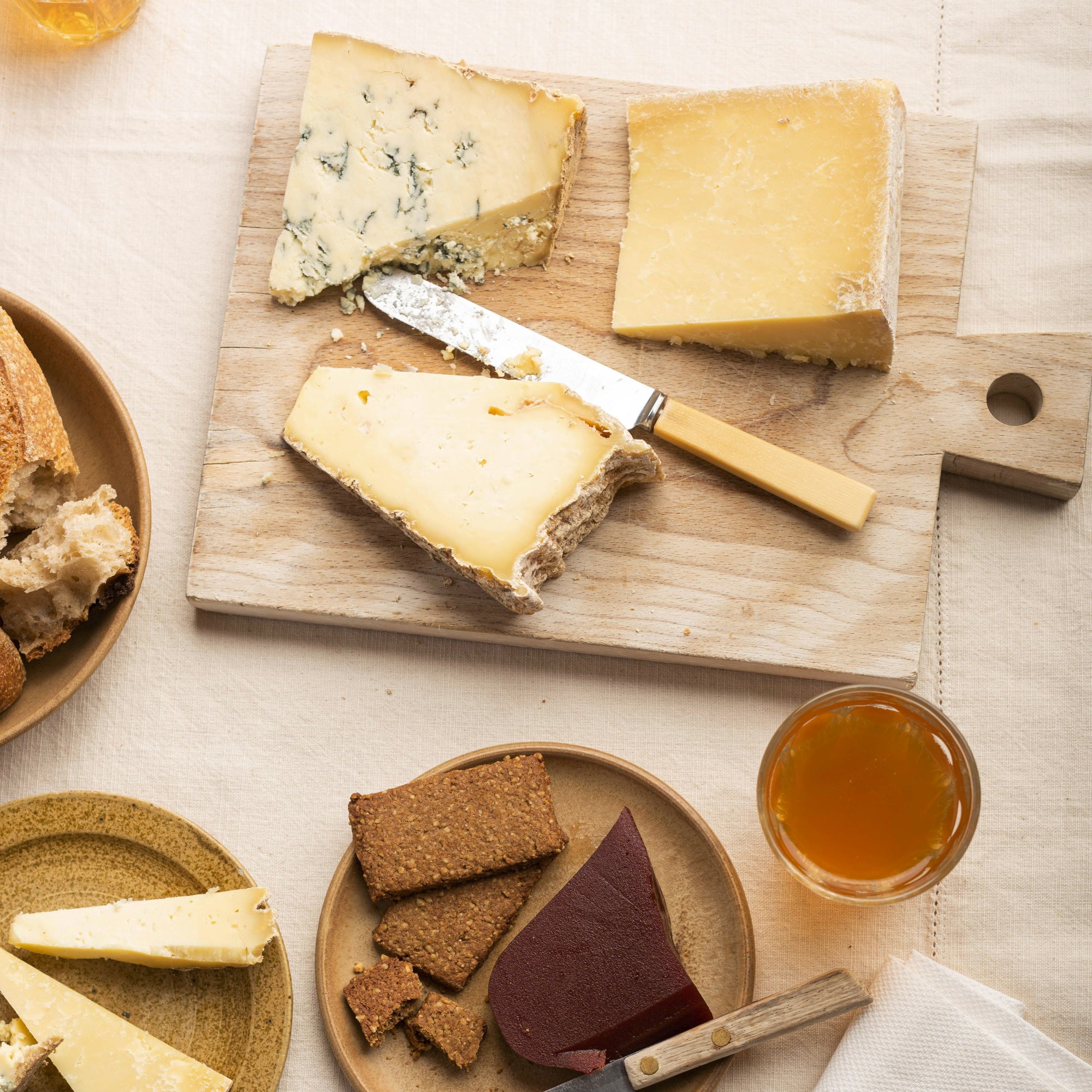 A board of three cheeses, with a knife alongside plates of cheese and biscuits.