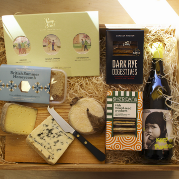 A selection of cheese, chocolates, biscuits and honey, on a wooden board with a cheese knife.