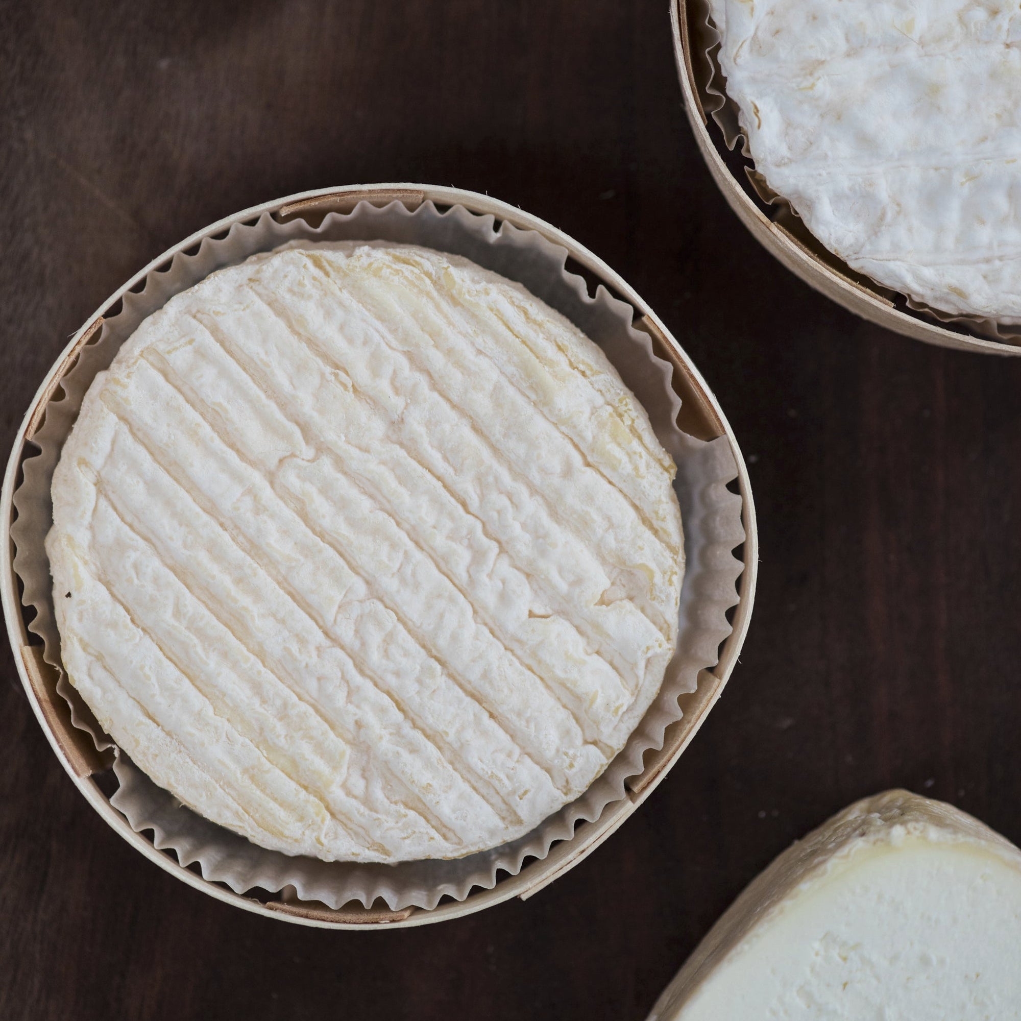 Multiple rounds of cheese in wooden trays on a dark surface.
