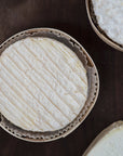 Multiple rounds of cheese in wooden trays on a dark surface.