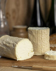 Large cut pieces of St. Tola goat's cheese and a knife on a wooden board.
