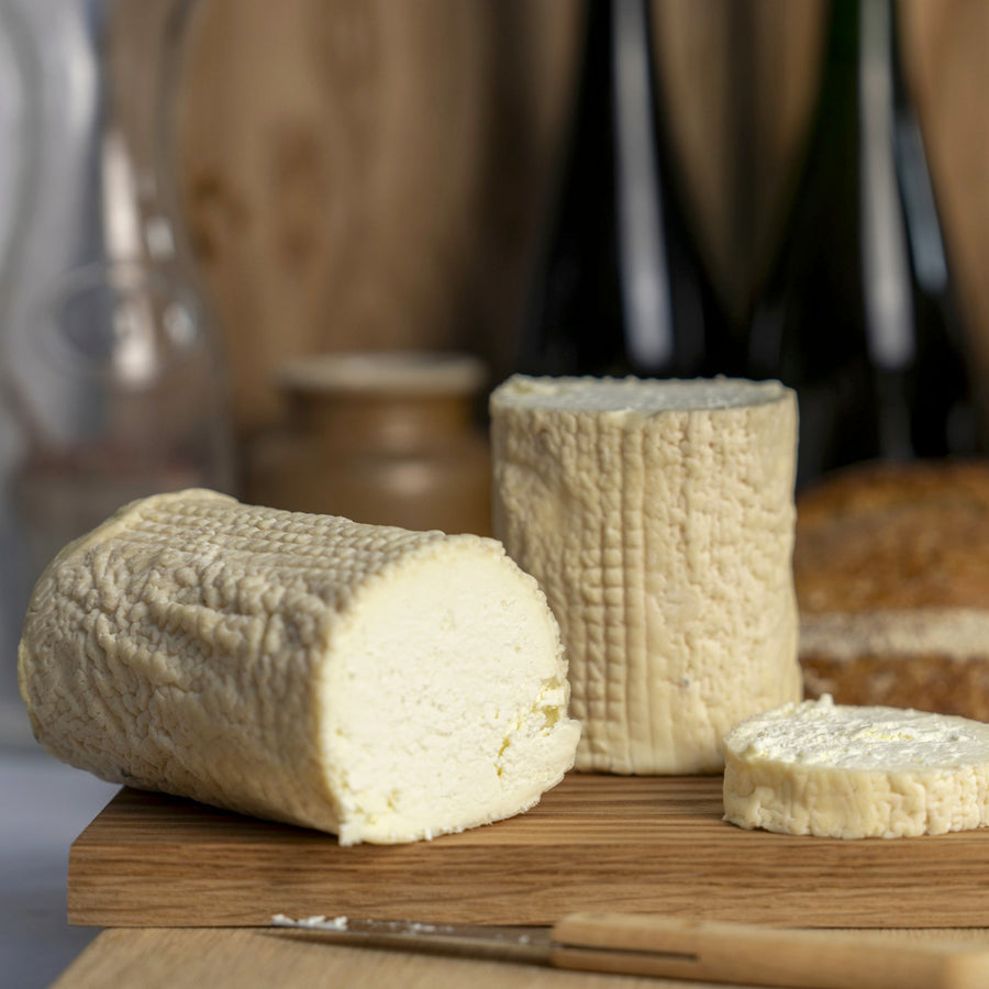 Large cut pieces of St. Tola goat's cheese and a knife on a wooden board.