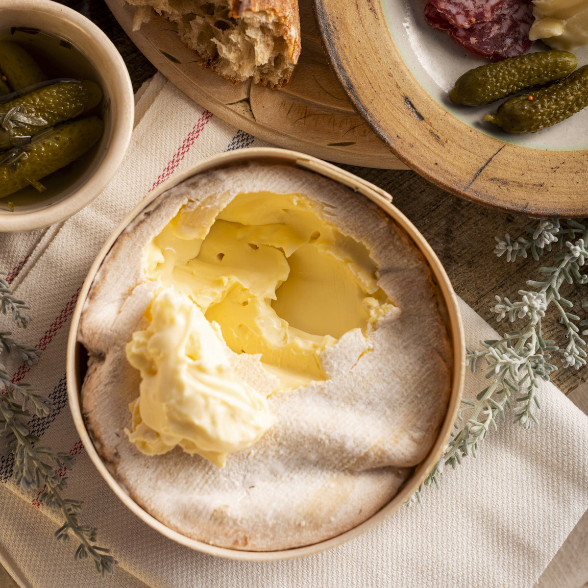Vacherin cheese with bread, salami, and pickles on a wooden board.