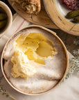 Vacherin cheese with bread, salami, and pickles on a wooden board.
