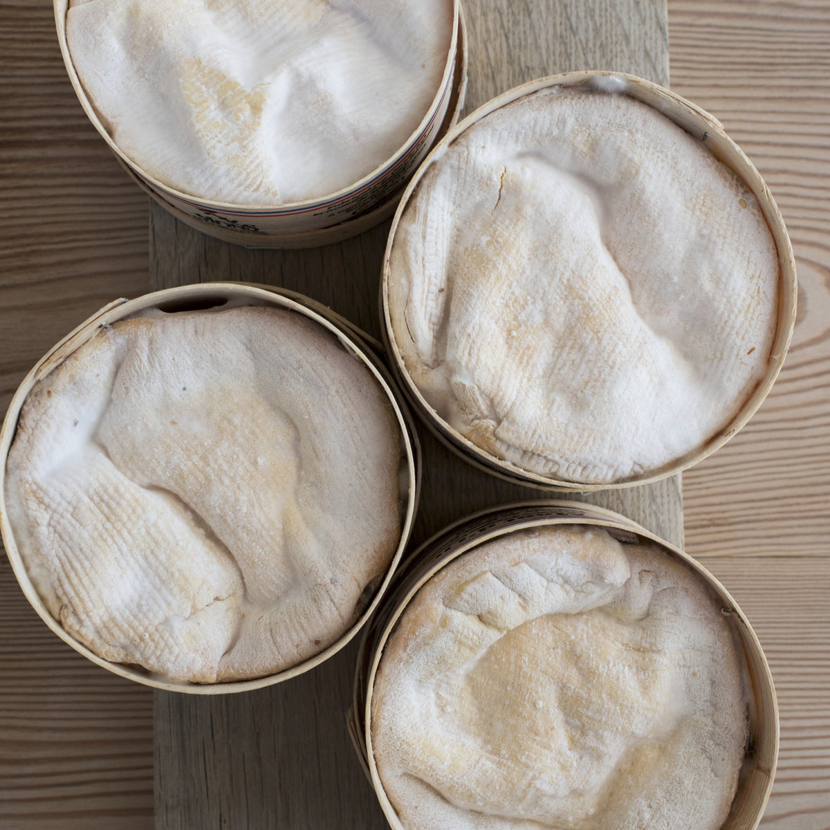 Four round boxes of Vacherin cheese on a wooden surface