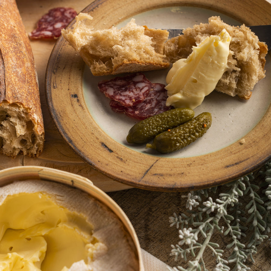 Platter with bread, butter, and cured meats on a wooden surface