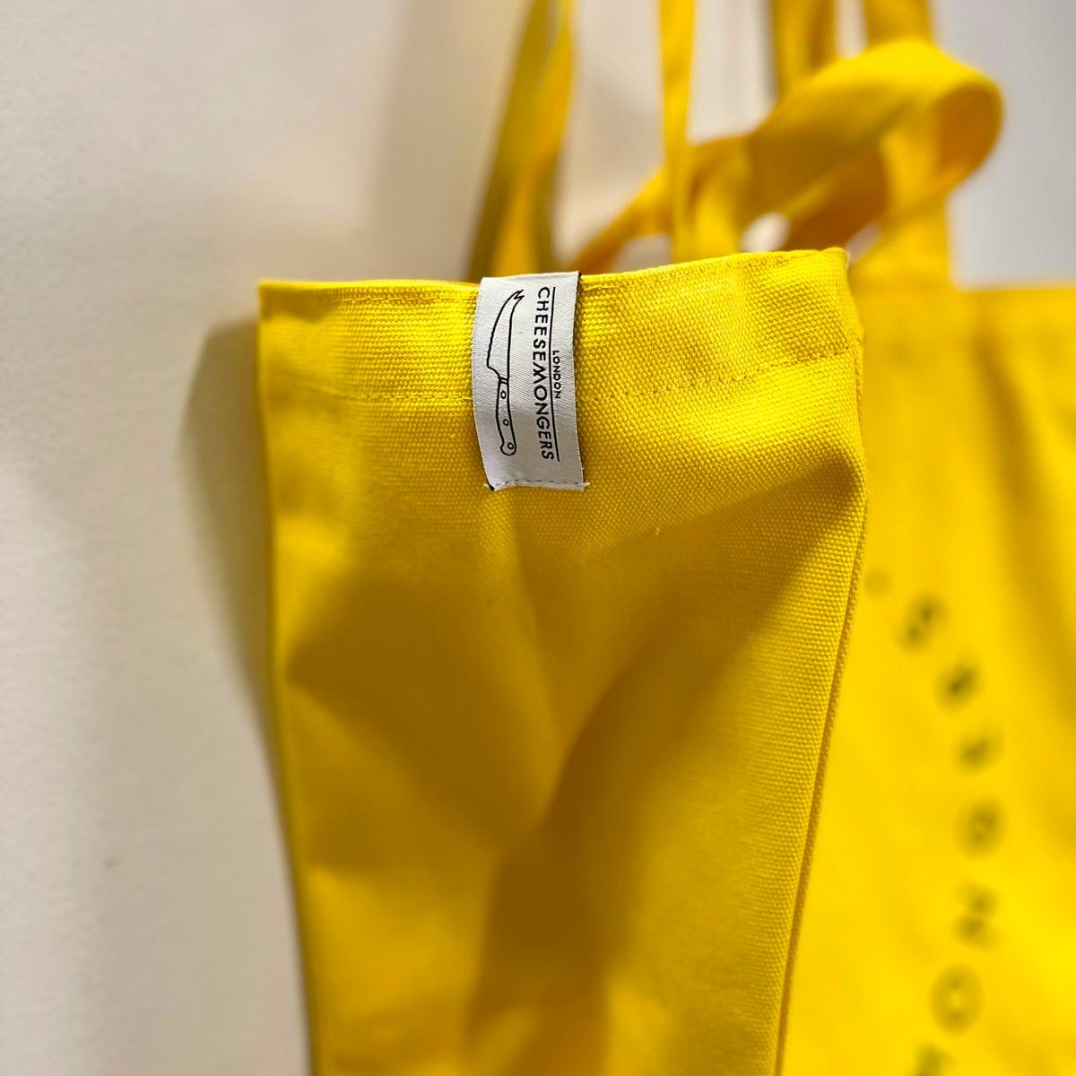 A close up of the branded label on a yellow canvas tote bag.