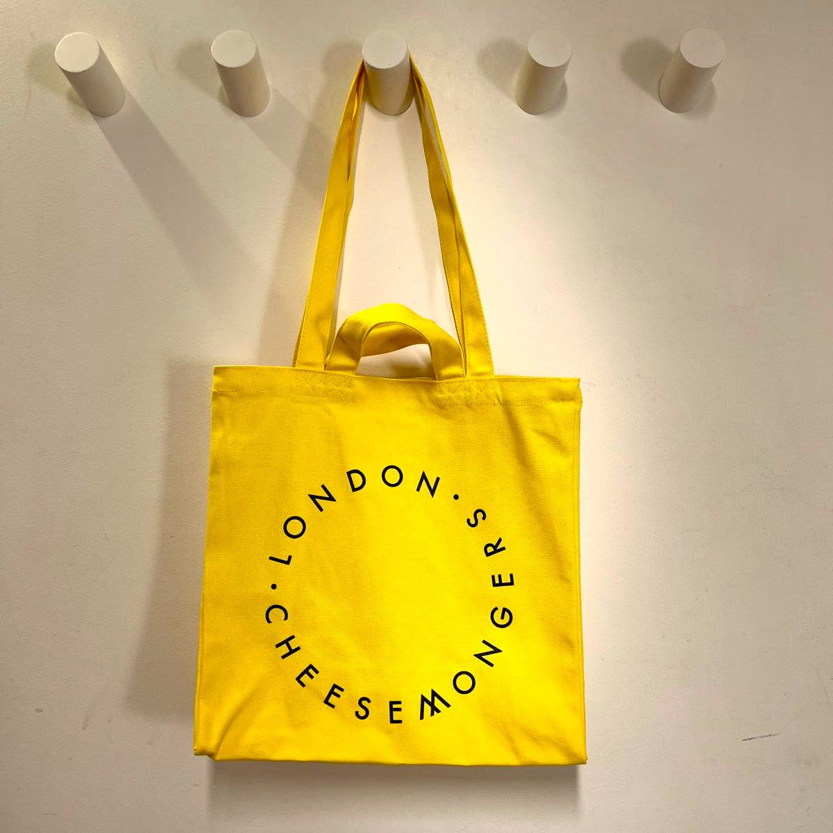 The yellow canvas London Cheesemongers tote bag hanging on the wall.