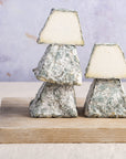 A stack of cut and whole blackmount goat cheese on a wooden board.