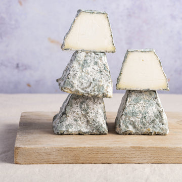 A stack of cut and whole blackmount goat cheese on a wooden board.