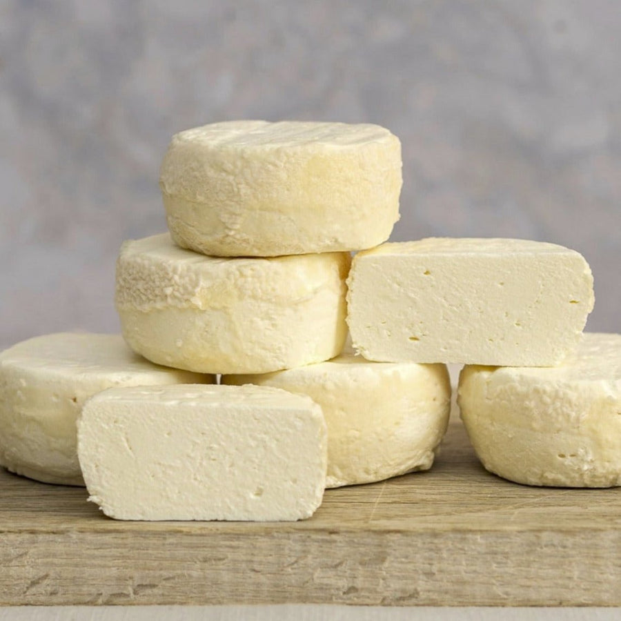 Cut and whole pieces of Castillon Frais fresh goat's cheese on a wooden board.