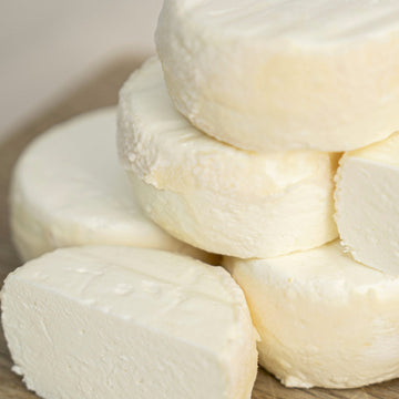 Close up of cut and whole pieces of Castillon Frais fresh goat's cheese on a wooden board.