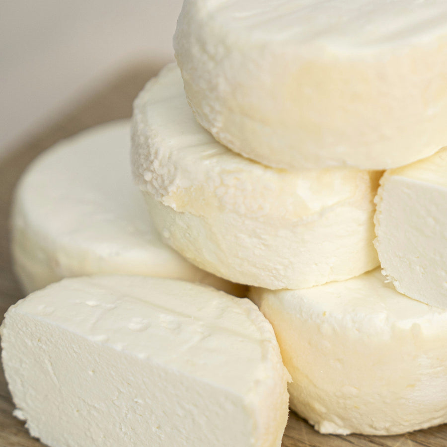 Close up of cut and whole pieces of Castillon Frais fresh goat's cheese on a wooden board.