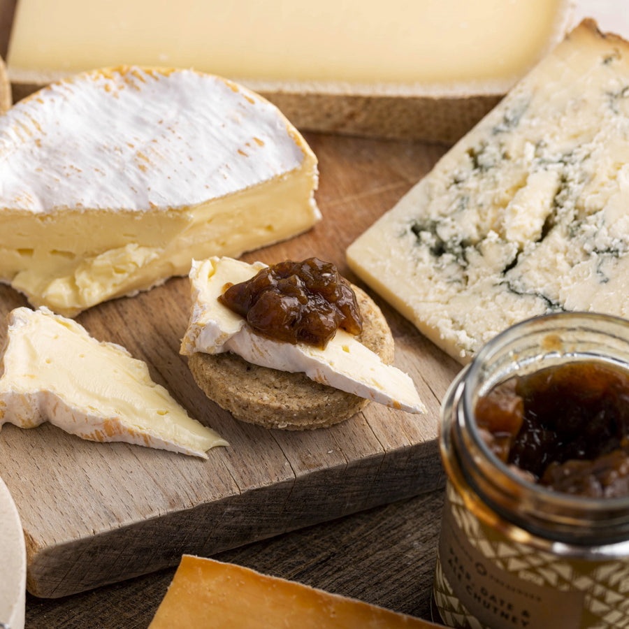 A selection of cheeses on a wooden board with biscuits and chutney.