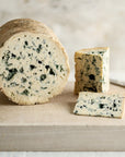 Large and small cuts of Fourme d'Ambert blue cheese on a wooden board.